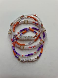 Set of five Clemson University handcrafted beaded bracelets celebrating college spirit! Each bracelet showcases vibrant school colors and is personalized with your college's name. Perfect accessory to flaunt your school pride or a thoughtful gift. Embrace your college journey with these stylish and meaningful bracelets! School Spirit Letter Beads Bracelets Gift, School Spirit Beaded Bracelets With Letter Beads For Gifts, School Spirit Beaded Bracelet With Letter Beads As Gift, School Spirit Jewelry With Letter Beads For Gifts, Personalized Orange Beaded Bracelets As Gift, Personalized Orange Beaded Bracelets For Friendship, Personalized Orange Bracelets With Round Beads, Personalized Orange Round Bead Jewelry, Clemson Bracelet