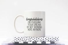 a white coffee mug sitting on top of a black and white checkered napkin with congratulations on it