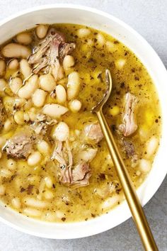 a white bowl filled with beans and meat on top of a table next to a spoon