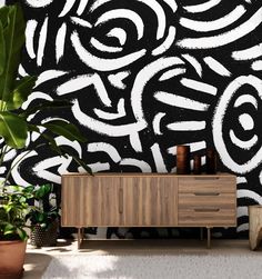 a black and white abstract wallpaper with wooden cabinet next to potted green plants