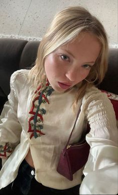 a woman sitting on top of a couch wearing a white shirt with red and blue trim