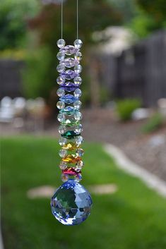 a colorful wind chime hanging from a string in the yard with grass and trees behind it