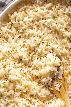 rice is being cooked in a pot with a wooden spoon and some parsley on the side