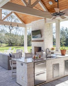 an outdoor kitchen with grill and sink under a wooden roof over looking a grassy area