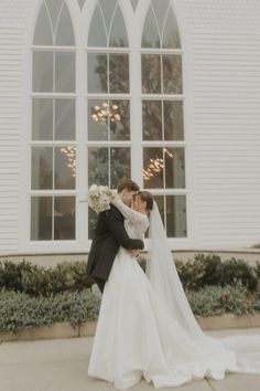 a bride and groom kissing in front of a white church with an arched window on the side