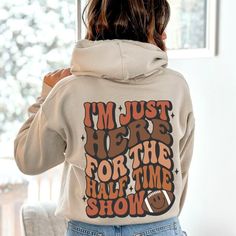 a woman wearing a hoodie that says i'm just here for the half time show