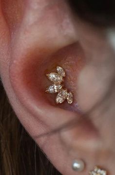 a woman's ear is adorned with three small gold leaves and pearled beads