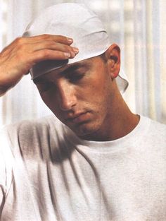 a man wearing a white hat is holding his hand to his head and looking down