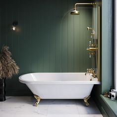 a white bath tub sitting in a bathroom next to a green wall with gold fixtures