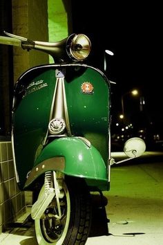 a green scooter parked in front of a building at night with its lights on