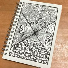 a spiral notebook with an intricate design on the cover, sitting on top of a wooden table