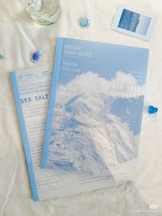 two blue and white papers sitting on top of a bed next to a glass bottle