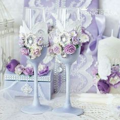 two wine glasses with flowers on them sitting next to a cake and candlesticks