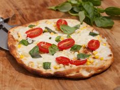 a pizza sitting on top of a wooden cutting board next to a knife and some leaves