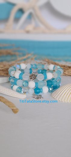 bracelets with blue and white beads are sitting on the sand next to a seashell