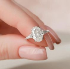 a woman's hand holding an engagement ring with a diamond in the middle and two diamonds on each side