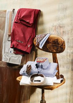 an old wooden chair with clothes hanging on the wall next to it and a pair of shoes