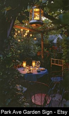 an outdoor dining area with table, chairs and lantern lights hanging from the tree branches