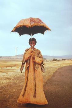 a woman with an umbrella standing on the side of a road in front of a field