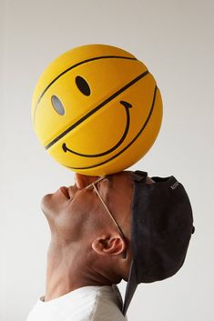 a man with a smiley face on his head holding a basketball over his head in the air