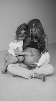 a pregnant woman is sitting on the floor with her two young daughters, both holding each other