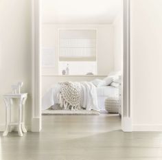 an open door leading to a bedroom with white furniture and decor on the floor, in front of a bed