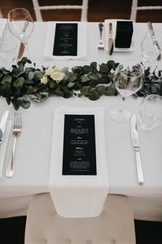 the table is set with white linens and greenery for an elegant wedding reception