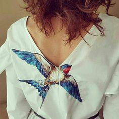 the back of a woman's white shirt with a bird painted on her chest