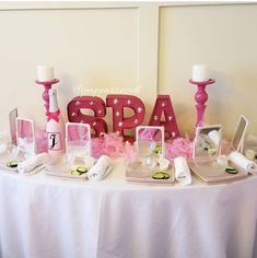 a table topped with pink candles and personalized items on top of a white table cloth