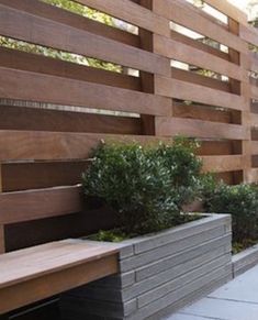 a wooden bench sitting in front of a wall next to a planter filled with trees