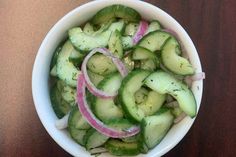 a white bowl filled with cucumbers and onions on top of a wooden table