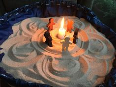 a candle is lit in the sand with small figures on it