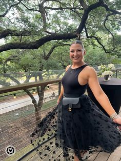 a woman standing on a deck wearing a black dress and holding her hand in her pockets