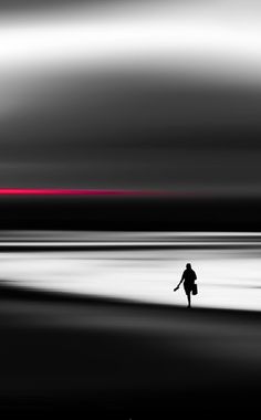 a lone person walking on the beach in black and white with a red line behind them