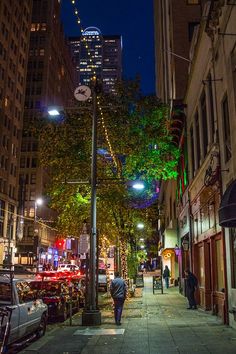 a city street at night with cars parked on the side and people walking down the sidewalk