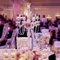 an elegant centerpiece is surrounded by candles and flowers on a table in a banquet hall