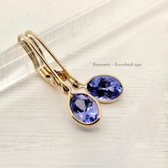 A Violet purple blue oval Tanzanite in a simple 14k gold bezel suspended from your choice of, lever backs, thin round hoops, or diamond tops. Select the style you love the most. All made with ethical genuine gemstones and recycled solid 14k gold Genuine Tanzanite approximately .60 - .70 carats each oval-cut 6.5 x 4.5 mm Blue Violet to periwinkle - colors vary Diamonds option: .05 each diamond hoop Solid 14 karat yellow gold Made to order - 1 week production time Select your option: :: Style 1: T Oval Tanzanite Earrings, Tourmalated Quartz Ring, Unique Diamond Wedding Bands, Watermelon Tourmaline Ring, Diamond Tops, Pink Sapphire Ring Engagement, Tourmalated Quartz, December Birthstone Ring, Tanzanite Earrings