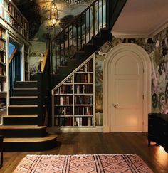 a room with stairs, bookshelves and rugs on the wooden flooring