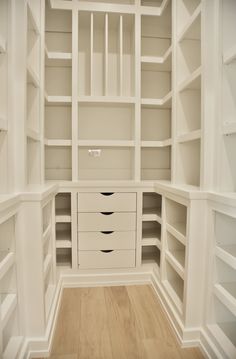 an empty walk in closet with white shelving and wood flooring on the side