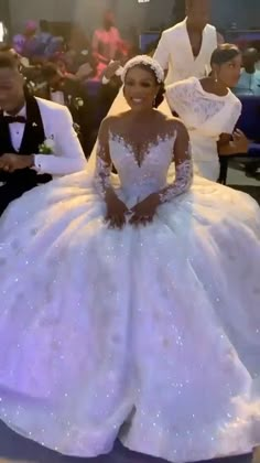 a woman in a white wedding dress sitting on the floor with other people behind her