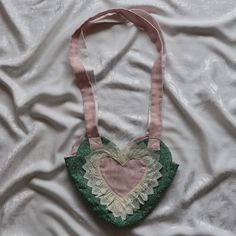 a heart shaped purse is laying on a white sheet with pink and green trimmings