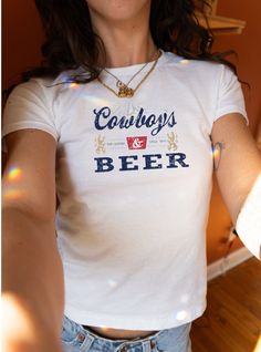 Saddle up for style with our 'Cowboys & Beer' Women's Baby Tee, inspired by the timeless charm of the Old West. This vintage-style tee captures the essence of cowboy culture and the classic enjoyment of a well-deserved beer. With its eye-catching distressed graphic, it evokes the nostalgia of the legendary year 1873. Crafted from the reliable comfort of the Gildan 5000B, this shirt is tailored to fit the modern cowgirl. It's not just apparel--it's a tribute to the stories and the history that sh Vintage Unisex Text Print Tops, Vintage Text Print Unisex Tops, Unisex Vintage Tops With Text Print, Unisex Vintage Text Print Tops, Vintage Graphic Print Tops For Game Day, Fitted Cotton T-shirt For Game Day, Vintage Fitted T-shirt With Logo Print, Fitted Vintage T-shirt With Logo Print, Vintage Short Sleeve Tops For Game Day