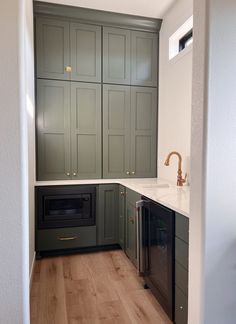 an empty kitchen with green cabinets and white counter tops, wood flooring in the foreground