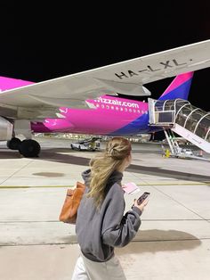 a woman is walking towards an airplane with luggage in her hand and looking at her cell phone