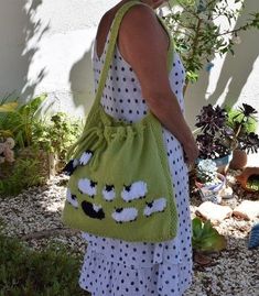 a woman carrying a green bag with black and white sheep on it's side