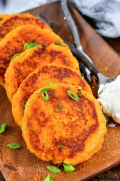 three sweet potato cakes on a wooden cutting board with whipped cream and green leaves next to it