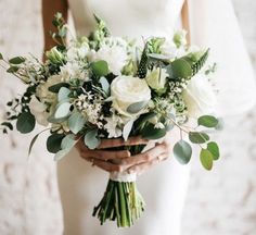 a bride holding a bouquet of white flowers and greenery