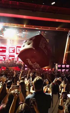 a large group of people at a concert with their hands in the air and one person holding up a giant red object