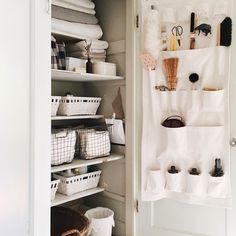 an organized closet with white linens, baskets and other items on shelves in it