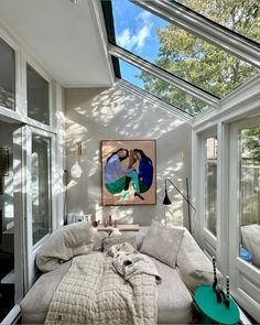 a bed sitting under a skylight in a bedroom next to two large windows and a painting on the wall